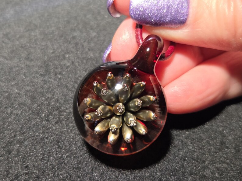 Round glass pendant featuring a dimensional metallic floral design with raised golden petals and a rich red backing, shown against a dark background for contrast.
