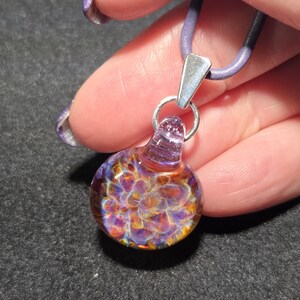 Handmade lampwork pendant with shimmering purple and amber frit implosion, set on a sterling silver bail and purple cord.