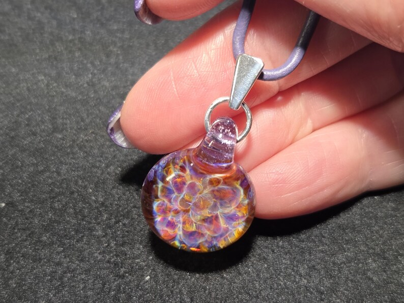 Handmade lampwork pendant with shimmering purple and amber frit implosion, set on a sterling silver bail and purple cord.
