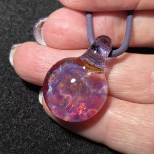 Dainty hand blown borosilicate glass implosion pendant with sparkling pink, purple, blue and amber frit, shown against the artist’s hand.