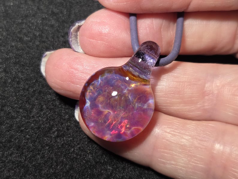 Dainty hand blown borosilicate glass implosion pendant with sparkling pink, purple, blue and amber frit, shown against the artist’s hand.