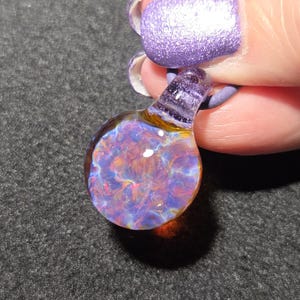 Dainty boro glass choker pendant showing a detailed flower-like implosion with shimmering violet, blue, magenta and amber colors that change with the background.