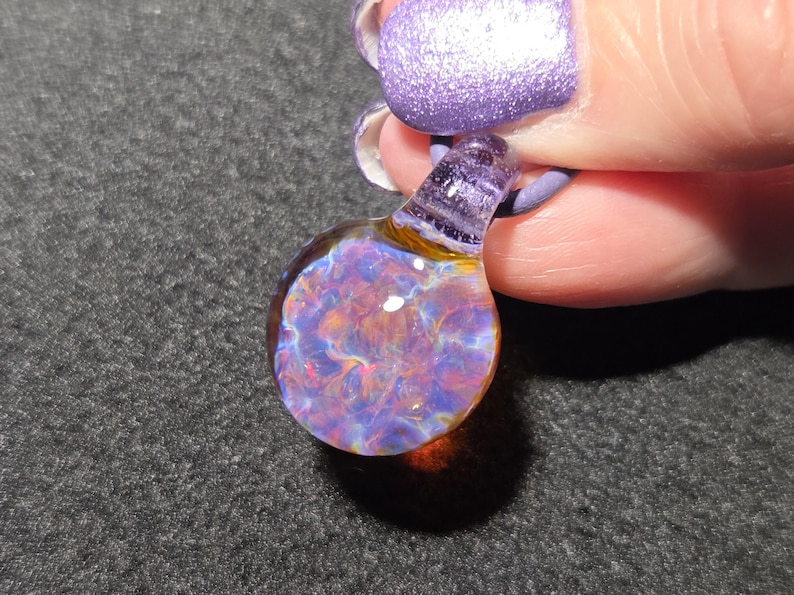 Dainty boro glass choker pendant showing a detailed flower-like implosion with shimmering violet, blue, magenta and amber colors that change with the background.
