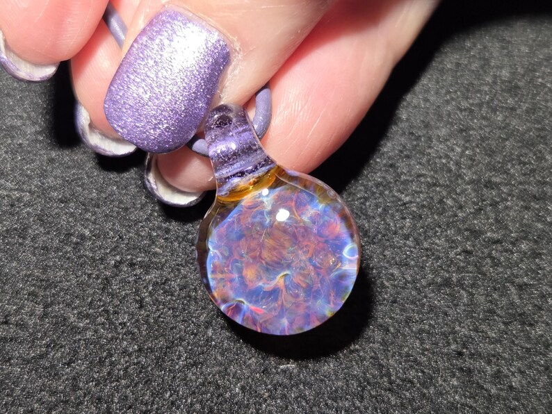Sparkly handmade borosilicate pendant with a colorful frit implosion, purple glass bail and luminous blue, pink and gold details against black.