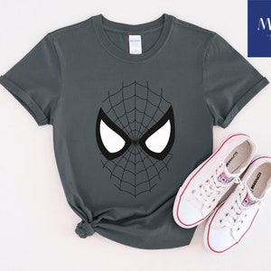 Pu&ograve; includere: T-shirt grigio scuro con un design a ragnatela nera e forme di occhi bianchi. La maglietta &egrave; abbinata a scarpe da ginnastica Converse bianche con dettagli rossi. L'immagine include il testo "MAK PRINTING STORE".