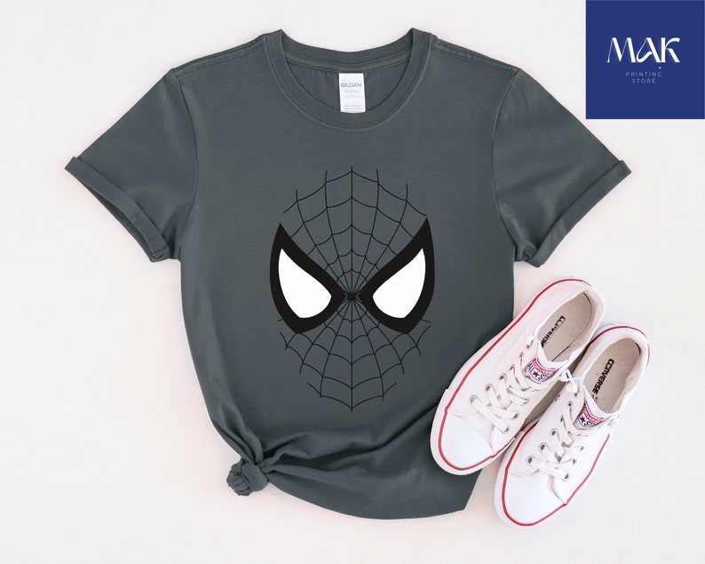 Pu&ograve; includere: T-shirt grigio scuro con un design a ragnatela nera e forme di occhi bianchi. La maglietta &egrave; abbinata a scarpe da ginnastica Converse bianche con dettagli rossi. L'immagine include il testo "MAK PRINTING STORE".