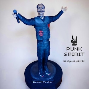May include: A 3D-printed figurine of Corey Taylor, the lead singer of Slipknot, in a dark blue outfit, holding a microphone. The figurine stands on a black base with the band's logo and the singer's name. The text "PUNK SPIRIT" is also visible.