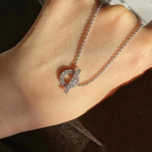 May include: A delicate silver necklace with a pendant. The pendant has a circular design and a bar closure, both encrusted with small, sparkling stones. The chain is fine and the pendant is centered. The necklace is displayed against a neutral background.