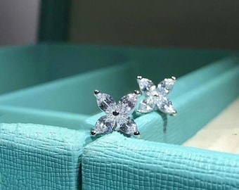May include: A pair of silver stud earrings with a flower design featuring clear cubic zirconia stones.