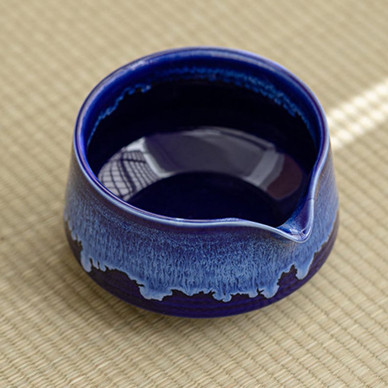 May include: A small, blue ceramic teacup with a white glaze on the rim and a spout. The cup is designed for pouring tea.