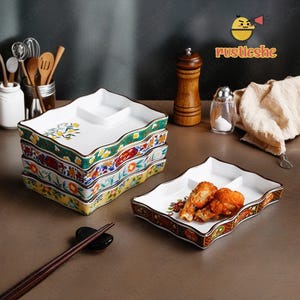 May include: A set of four white ceramic serving dishes with colorful floral patterns. The dishes have three compartments and are stacked on top of each other. The dishes are on a light brown surface with a smaller dish containing fried food.