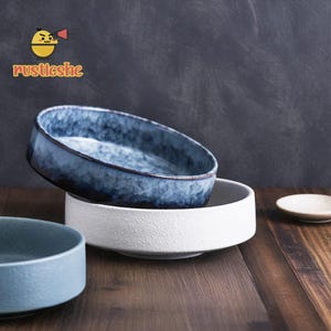 Könnte beinhalten: Drei Keramikschalen in verschiedenen Blautönen. Die oberste Schale ist dunkelblau mit einer marmorierten Glasur. Die mittlere Schale ist weiß mit einer strukturierten Oberfläche. Die unterste Schale ist hellblau mit einer glatten Oberfläche.