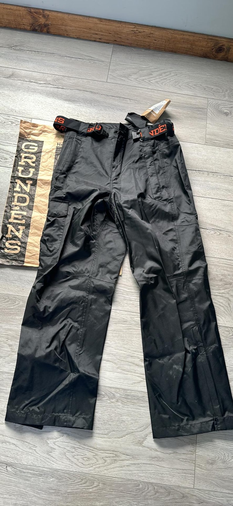 Puede incluir: Pantal&oacute;n cargo negro con cintur&oacute;n negro y texto naranja que dice "GRUNDENS" en la pierna izquierda y "NDE" en la pierna derecha.