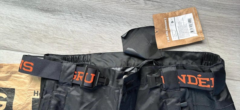 Puede incluir: Pantal&oacute;n de esqu&iacute; negro con una cintura el&aacute;stica naranja y negra. La cintura tiene las palabras "GR&Uuml;NDER" e "INS" impresas en ella.