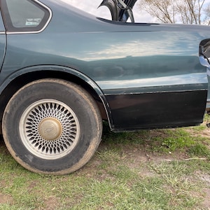 May include: A dark green Chevrolet Caprice sedan with a black bumper and a silver wheel with a Chevrolet logo. The car is parked on a grassy surface.