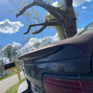 Könnte beinhalten: Ein dunkelblaues Auto mit einem Heckspoiler und einem roten Rücklicht. Das Auto ist vor einem Haus und einem Briefkasten geparkt.