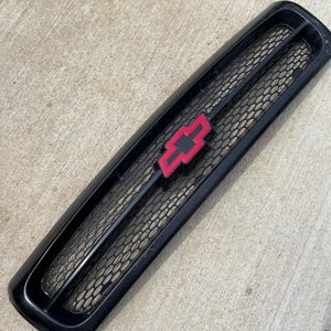 Peut inclure: Calandre de voiture en plastique noir avec un logo Chevrolet rouge. La calandre a un motif en nid d'abeille.