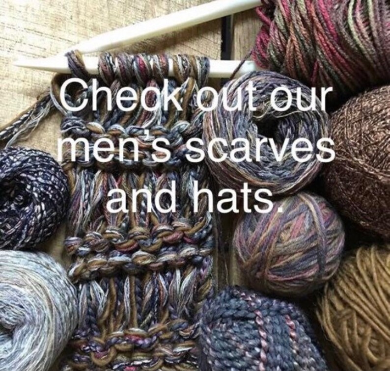 Puede incluir: Primer plano de una bufanda tejida con diferentes tonos de hilo marr&oacute;n, gris y blanco. La bufanda est&aacute; rodeada de ovillos de lana de diferentes colores y texturas. El texto "Check out our men's scarves and hats." es visible en la imagen.