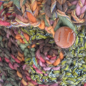 May include: Close-up of a brown button on a multi-colored knitted fabric. The fabric is made of a variety of yarns in shades of brown, green, orange, pink, and blue.