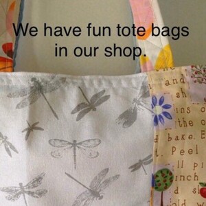 May include: A white tote bag with a dragonfly print. The bag has a patchwork design with a yellow, pink, and blue floral pattern. The text "We have fun tote bags in our shop." is printed on the bag.
