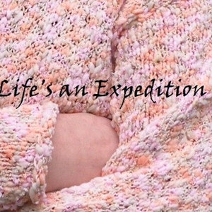 Puede incluir: Primer plano de un c&aacute;rdigan de punto rosa y melocot&oacute;n con un aspecto texturizado y esponjoso. El c&aacute;rdigan est&aacute; doblado y el texto "Life's an Expedition" es visible en la tela.