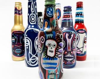 May include: A collection of six glass bottles, each painted with colorful, abstract designs. The bottles are decorated with various patterns, including stripes, dots, and swirls. One bottle features a skull and crossbones design. The bottles are all different colors, including blue, red, gold, and green.