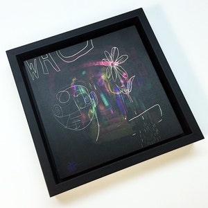 May include: A black framed canvas with a white line drawing of a face and a flower on a dark background with iridescent paint splatters. The text "WHO" is written in white on the top left corner of the canvas.