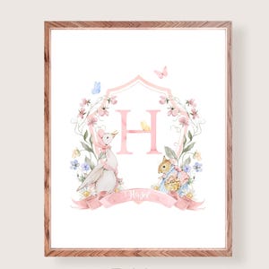 Pode incluir: Impressão em aquarela emoldurada com a letra rosa "H" rodeada por elementos florais e ilustrações de animais. Uma faixa na parte inferior diz "Hazel". A obra de arte tem uma paleta de cores pastel e uma moldura de madeira.