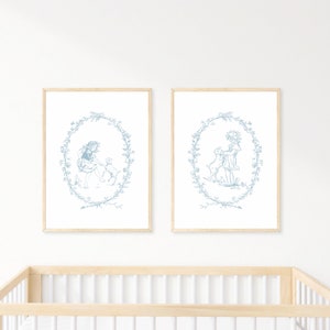 May include: Two framed prints with a blue and white design of a girl with a dog in a wreath. The prints are hanging on a white wall above a wooden crib.
