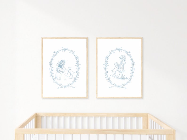 May include: Two framed prints with a blue and white design of a girl with a dog in a wreath. The prints are hanging on a white wall above a wooden crib.