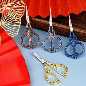 May include: Four pairs of decorative scissors with ornate handles. The scissors are in gold, bronze, blue, and iridescent colors.