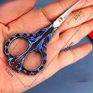 May include: Blue metal scissors with an ornate design, measuring 5.5 inches long and 3.7 inches wide.
