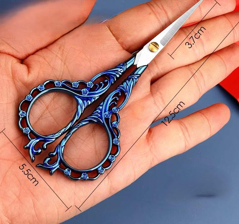 May include: Blue metal scissors with an ornate design, measuring 5.5 inches long and 3.7 inches wide.