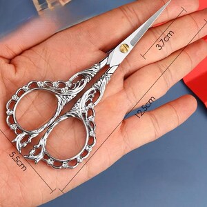 May include: Silver decorative scissors with a floral design and rhinestones. The scissors are 5.5 inches long and 3.7 inches wide.
