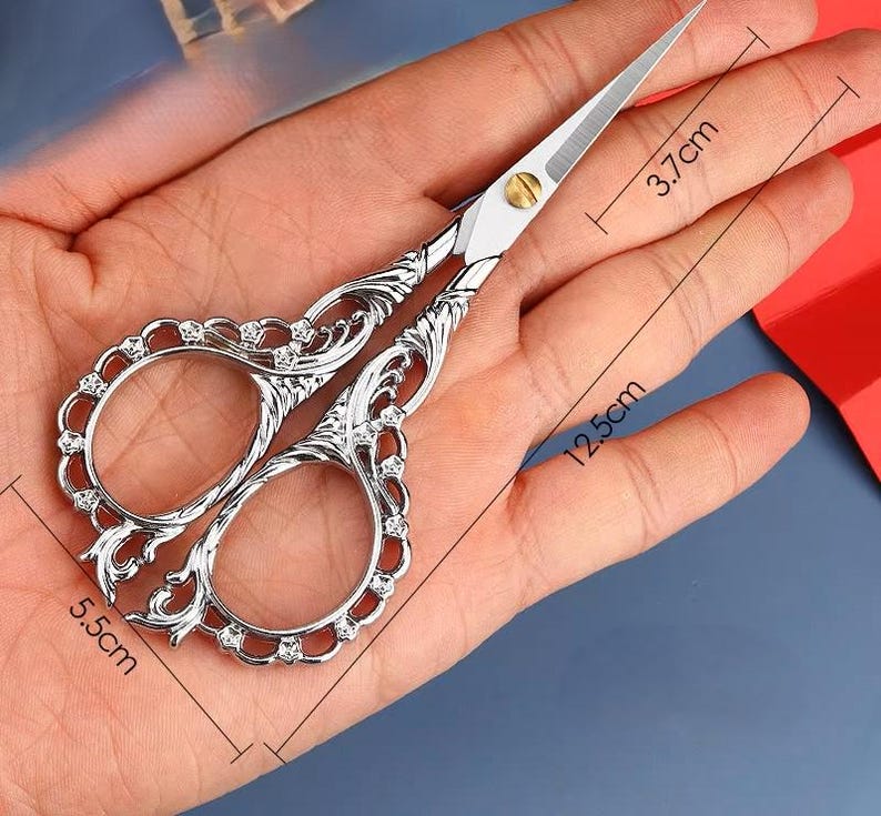 May include: Silver decorative scissors with a floral design and rhinestones. The scissors are 5.5 inches long and 3.7 inches wide.