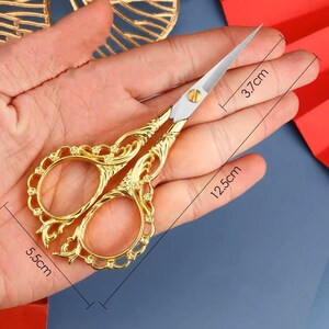 May include: Gold-toned decorative scissors with ornate details. The scissors are 5.5 inches long, 12.5 inches wide, and 3.7 inches tall.