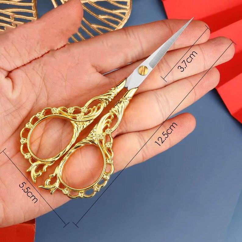 May include: Gold-toned decorative scissors with ornate details. The scissors are 5.5 inches long, 12.5 inches wide, and 3.7 inches tall.