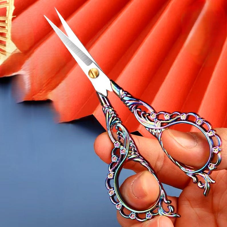 May include: A pair of small, ornate scissors with a rainbow iridescent finish. The handles are decorated with a floral design and rhinestones.