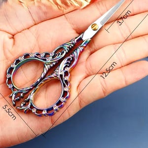 May include: A pair of ornate rainbow-colored scissors with a decorative design and rhinestones. The scissors are 5.5 inches long and 3.7 inches wide.