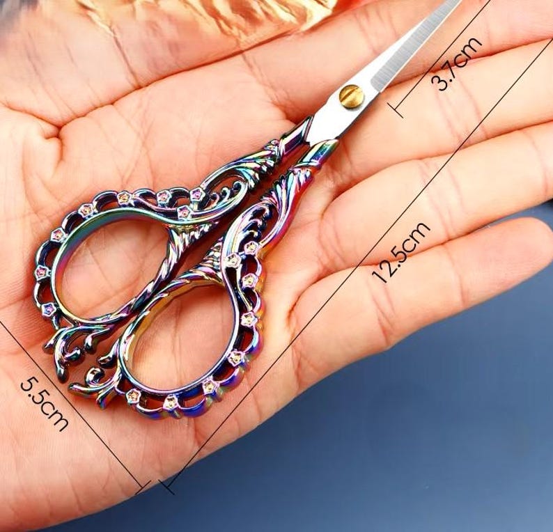 May include: A pair of ornate rainbow-colored scissors with a decorative design and rhinestones. The scissors are 5.5 inches long and 3.7 inches wide.