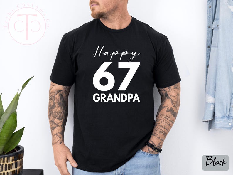 May include: Black t-shirt with the text "Happy 67 Grandpa" in white script and bold font. The number 67 is large and centered. The shirt is short-sleeved and appears to be made of cotton.