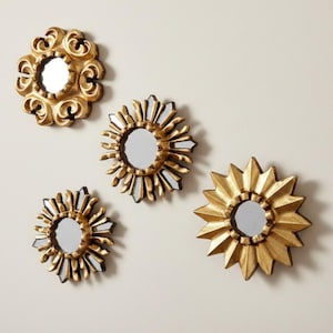 May include: A set of four circular wall mirrors with gold-toned frames. One mirror features an ornate, swirling scrollwork border, while the other three mirrors have sunburst-style frames with varying pointed and faceted ray designs.