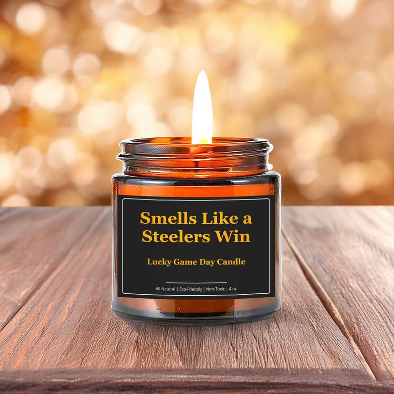 Wonderscape Wicks candle shop on Etsy presenting lit 4 oz amber jar soy wax candle with text smells like a Steelers win lucky game day candle on a wood table in a garden. Pittsburgh Football NFL sports gift for husband wife fiance boyfriend