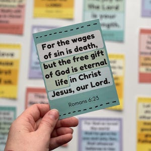 Puede incluir: Una tarjeta turquesa con el texto "Porque la paga del pecado es muerte, pero la d&aacute;diva de Dios es vida eterna en Cristo Jes&uacute;s, Se&ntilde;or nuestro. Romanos 6:23." La tarjeta se sostiene en una mano.