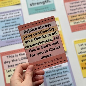 Puede incluir: Una mano sostiene una tarjeta rectangular con el texto "Regocijaos siempre, orad sin cesar, dad gracias en todo; porque esta es la voluntad de Dios para con vosotros en Cristo Jes&uacute;s." Otras tarjetas con texto est&aacute;n en el fondo.