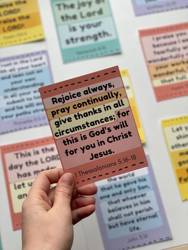 Puede incluir: Una mano sostiene una tarjeta rectangular con el texto "Regocijaos siempre, orad sin cesar, dad gracias en todo; porque esta es la voluntad de Dios para con vosotros en Cristo Jes&uacute;s." Otras tarjetas con texto est&aacute;n en el fondo.