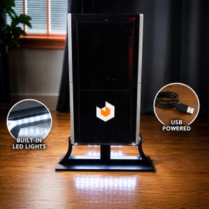 May include: A black and silver vertical tower display stand with a central orange and white geometric logo. The unit features built-in LED lights at the base and includes a black USB cable for power, as indicated by the text labels in the image.