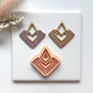 May include: Art Deco style earrings in mauve and tan with gold accents. The earrings have a geometric design with a diamond shape. A matching clay cutter is also shown in the image.