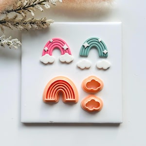 Puede incluir: Colección de cortadores de arcilla polimérica con forma de arcoíris y nube en rosa, verde azulado y naranja. Los cortadores de arcoíris tienen detalles de estrellas y las nubes son blancas. Ideales para manualidades y crear elementos decorativos.