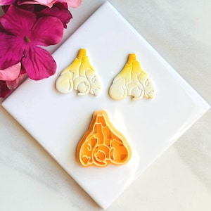 May include: Three yellow and white plastic cookie cutters shaped like a group of cats huddled together.